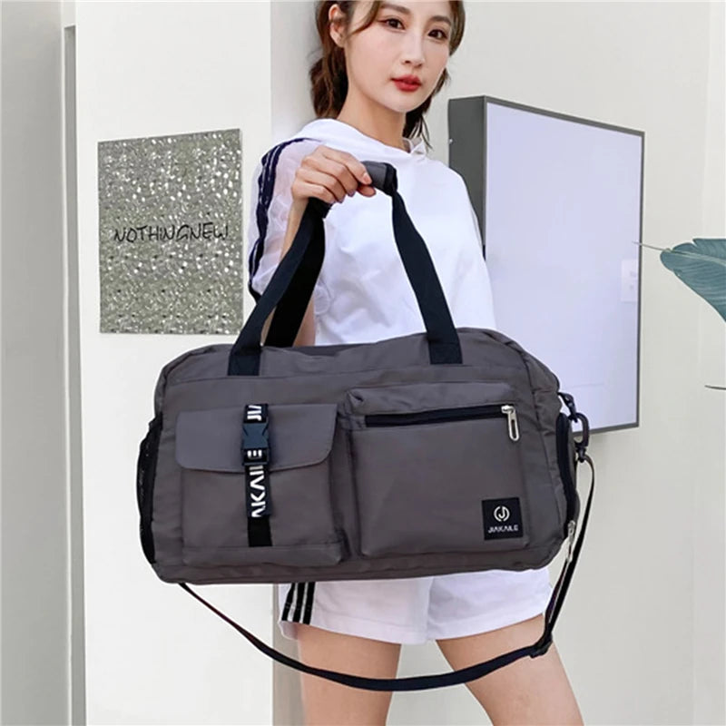 Gray women's travel handbag with multiple pockets and black handles held by woman in white outfit