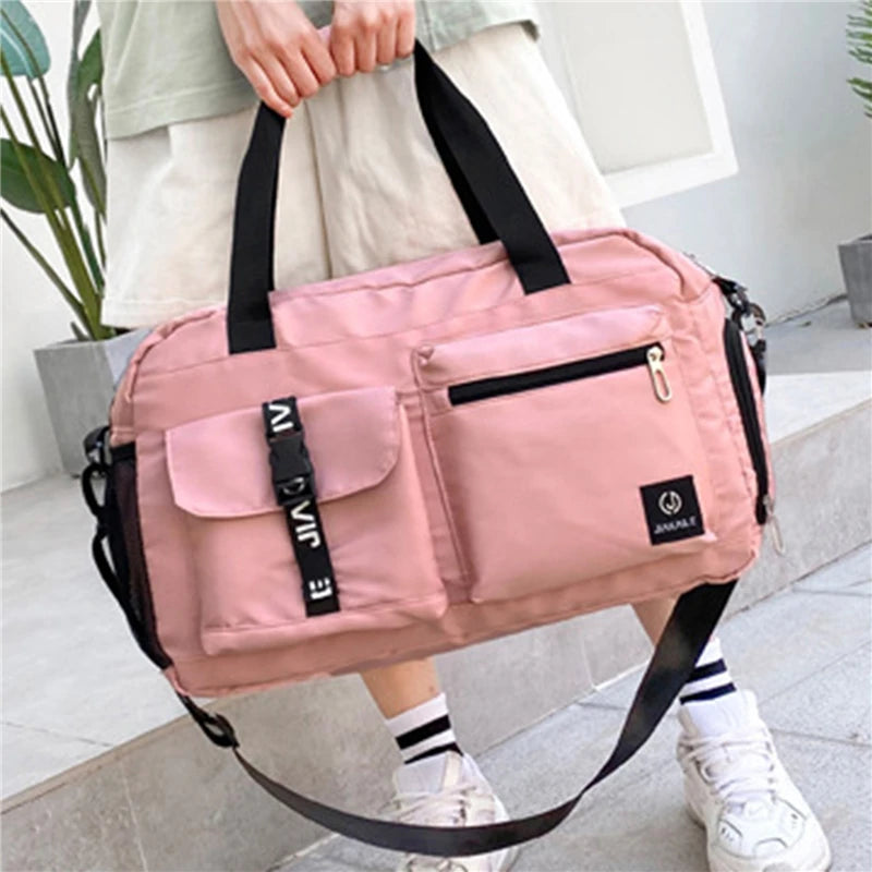Pink women's travel handbag with multiple pockets and black handles held by person outdoors