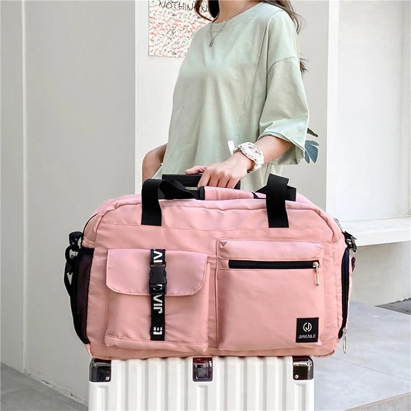 Pink women's travel handbag with multiple pockets carried over a white suitcase handle
