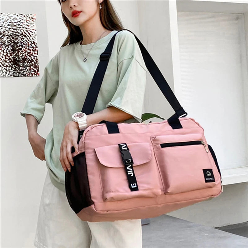 Pink women's travel handbag with multiple pockets and adjustable black strap carried by woman