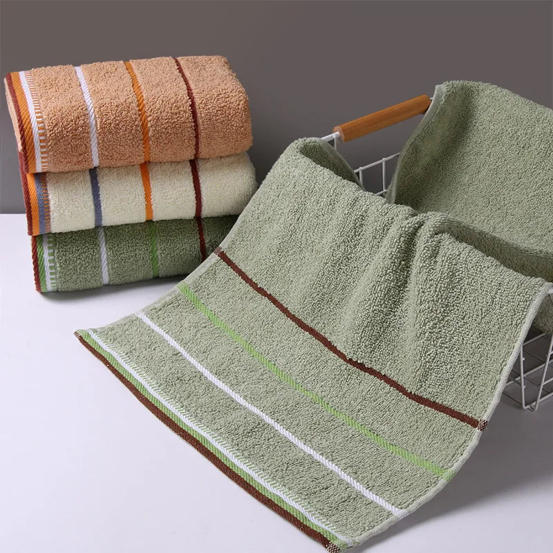 Set of pure cotton bath towels in green, beige, and brown colors with striped edges stacked and draped in a wire basket