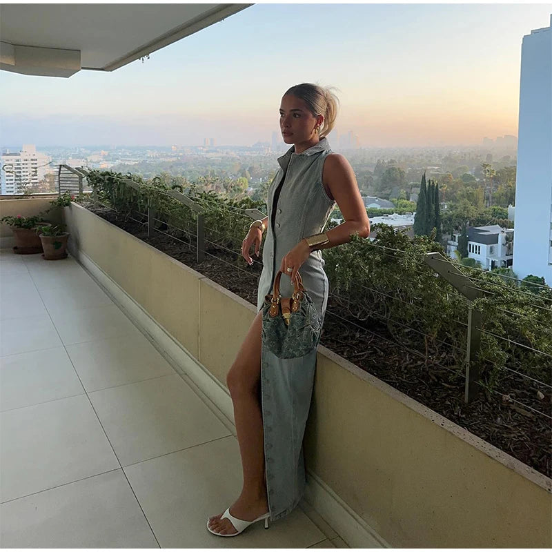 Woman wearing sleeveless women's jean long dress standing on terrace at sunset holding handbag